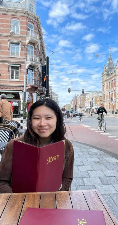 a student sitting on an outdoor restaurant patio with a menu in Amsterdam