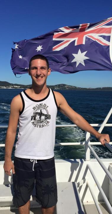 a student poses for a photo while on a boat with the Australian flag blowing behind them