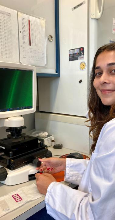 student in white coat sitting at desk in front of microscope and computer